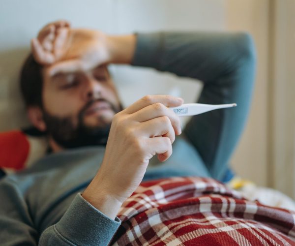 caucasian man staying in bed measuring temperature feeling sick