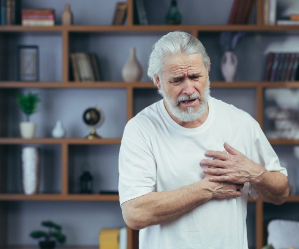 Gray-haired man has severe chest pain, grandfather's heart aches, holds hands on his chest, at home