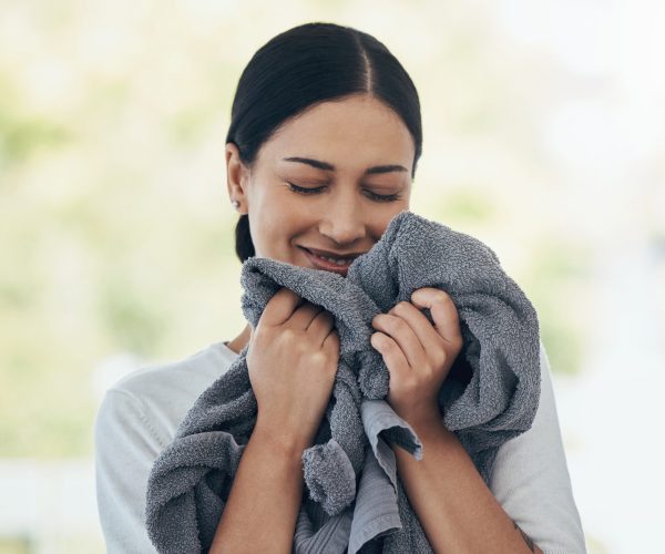 Laundry, fresh and woman smelling clean clothes with a smile, peace and calm in a house. Happy, young and smiling cleaner cleaning clothing, linen and towel in the morning with happiness in a home.