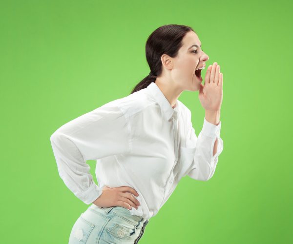 Do not miss. Young casual woman shouting. Shout. Crying emotional woman screaming on green studio background. Female half-length portrait. Human emotions, facial expression concept. Trendy colors
