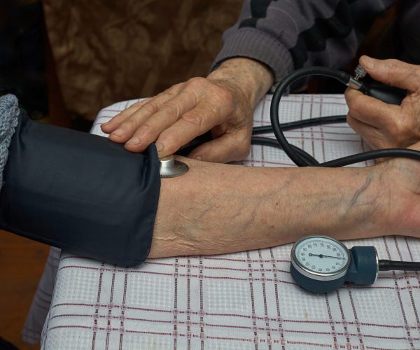 Measurement of blood pressure in the elderly with a manual blood pressure monitor. A tonometer and a phonendoscope are on hand. Horizontal frame.