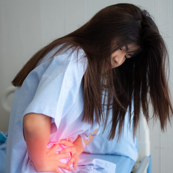 Unhappy Asian patient woman sitting on the hospital bed and holding on stomach suffering. Abdominal pain that comes from menstruation, diarrhea, or indigestion. Sickness and healthcare concept