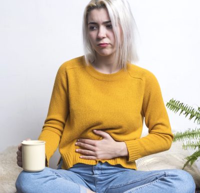 Young woman sitting at home holding a cup of tea while putting her hand in her stomach