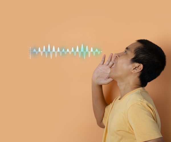 Young man shouting and screaming loud to side with hand on mouth with sound waves. Audio sound equalizer technology. orange studio background.