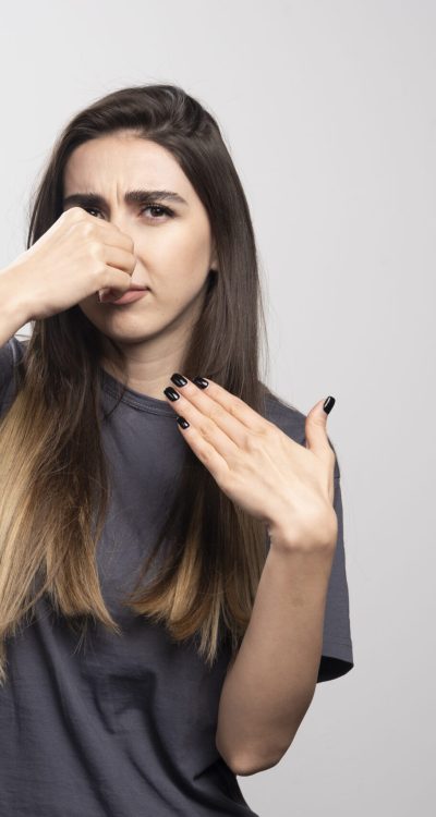 Young woman covering her nose with hand over a gray background. High quality photo