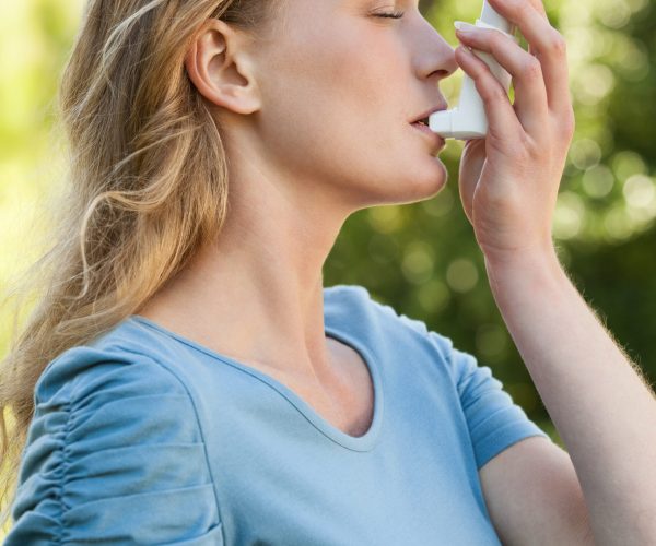 Side view of a young woman using asthma inhaler at the park